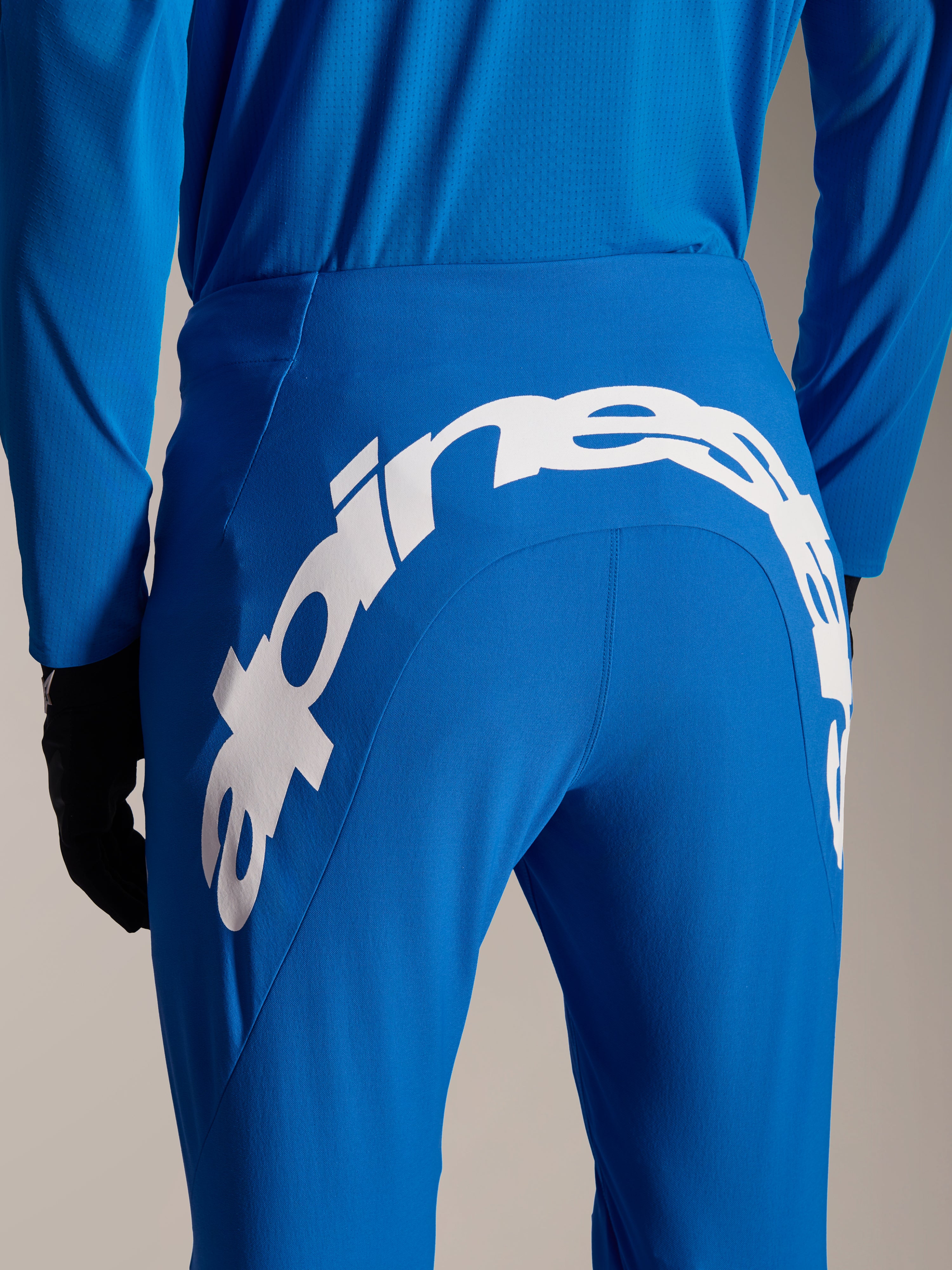 Alpinestars A-Supra Melt-byxor och tröja, blå MTB-utrustning, vy bakifrån med ett stort vitt Alpinestars-ordmärke på byxornas bakok, matchande långärmad tröja och svarta handskar
