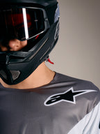 Alpinestars A-Supra Elite-tröja i gråtonat mikroperforerat tyg med vit logotyp och svart MTB-hjälm.