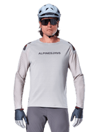 Alpinestars A-Aria Polartec Switch långärmad tröja, ljusgrå mountainbiketröja med laserperforeringar på ärmarna och logotyp på bröstet, bärs med ljusblå hjälm, solglasögon och grå handskar
