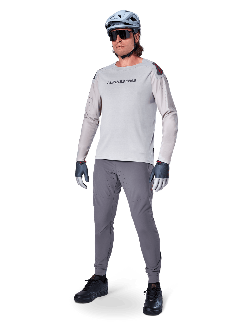 Alpinestars A-Aria Polartec Switch Jersey, långärmad MTB-tröja, ljusgrå, bärs tillsammans med mörkgrå mountainbike-byxor, hjälm och handskar, med laserperforerade ärmar och Alpinestars-logotyp på bröstet.