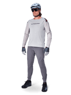 Alpinestars A-Aria Polartec Switch Jersey, långärmad MTB-tröja, ljusgrå, bärs tillsammans med mörkgrå mountainbike-byxor, hjälm och handskar, med laserperforerade ärmar och Alpinestars-logotyp på bröstet.