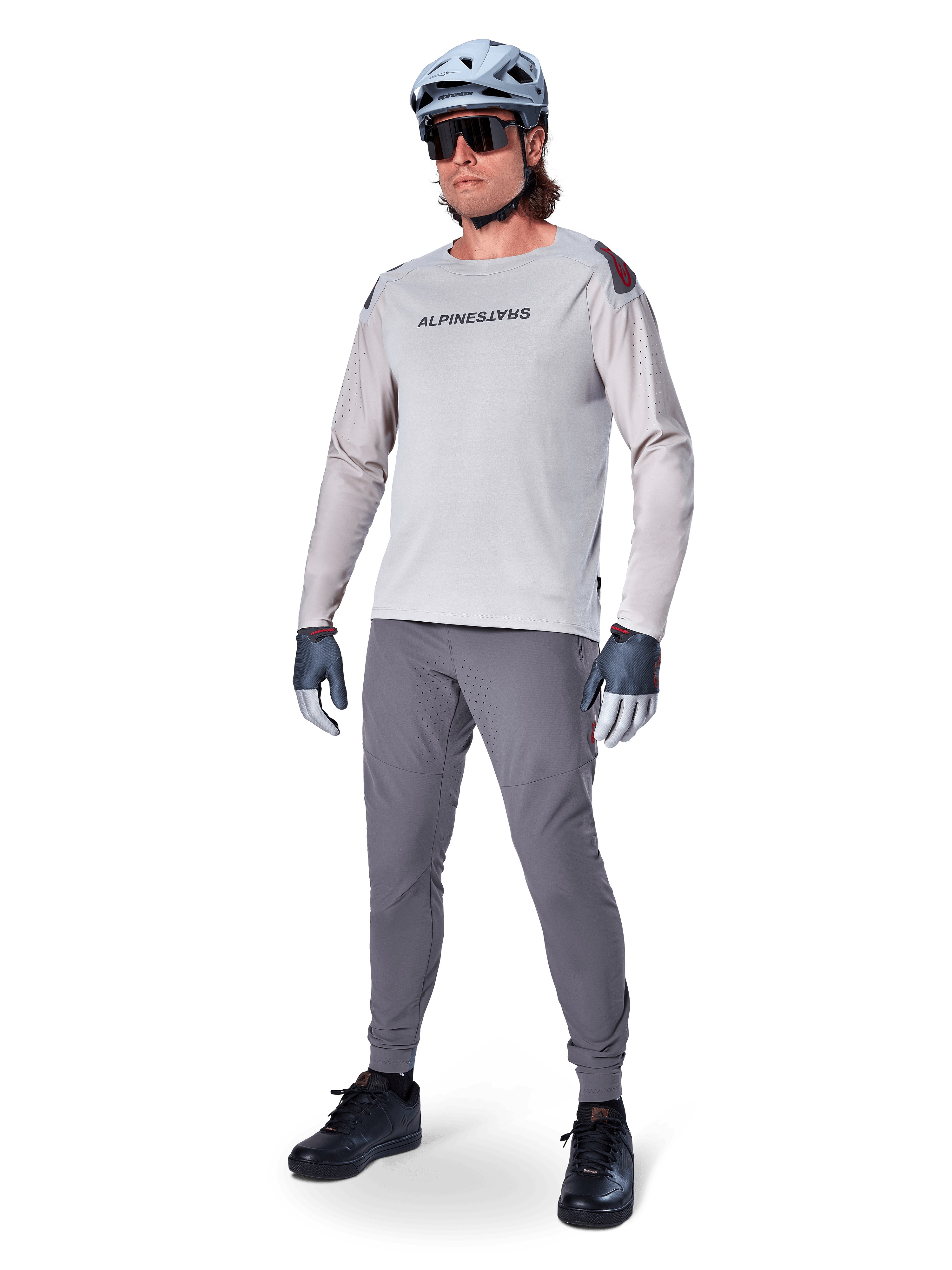 Alpinestars A-Aria Polartec Switch Jersey, långärmad MTB-tröja, ljusgrå, bärs tillsammans med mörkgrå mountainbike-byxor, hjälm och handskar, med laserperforerade ärmar och Alpinestars-logotyp på bröstet.