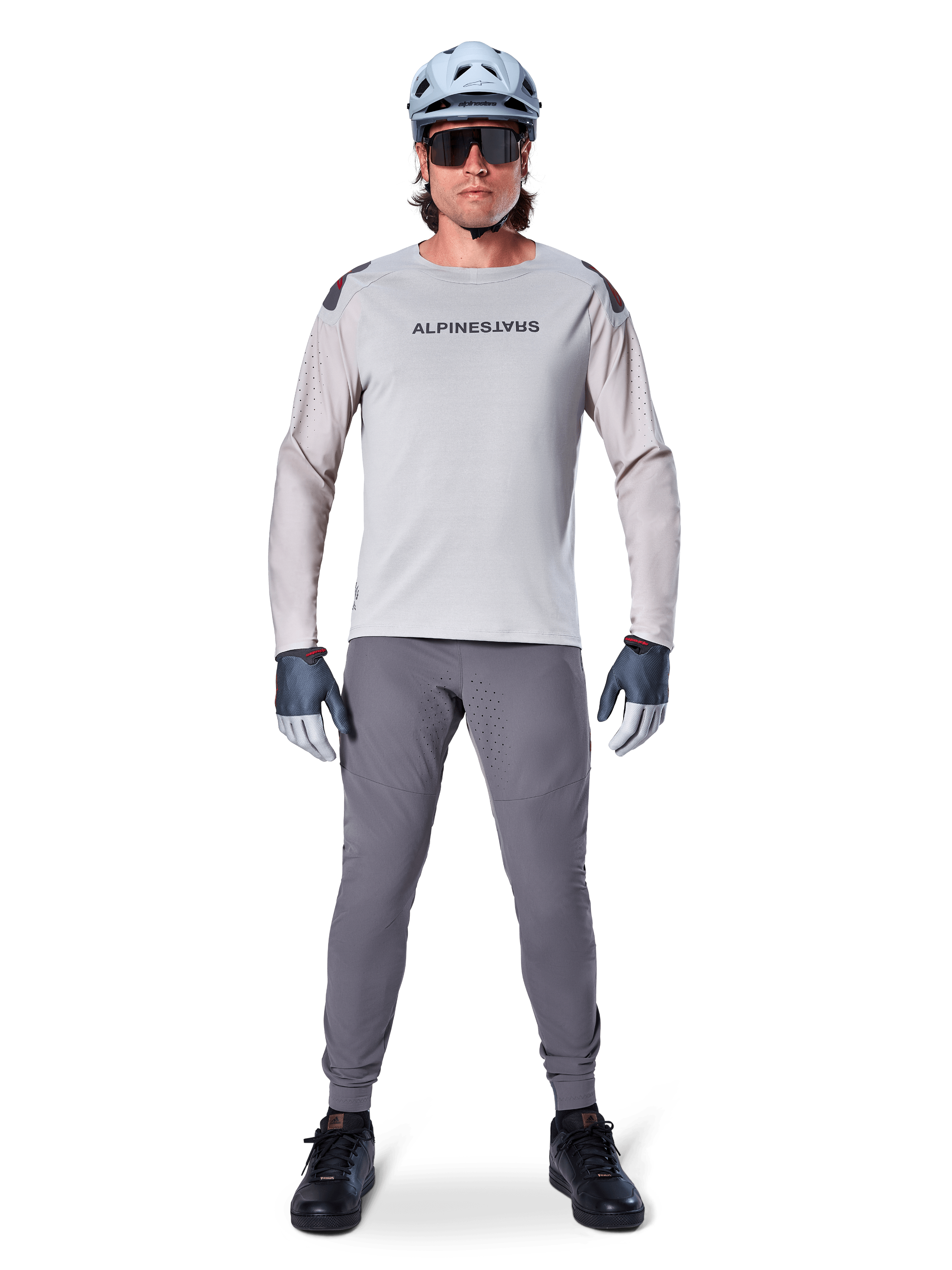 Alpinestars A-Aria Polartec Switch långärmad tröja, ljusgrå, bärs av en manlig mountainbikecyklist med mörkgrå MTB-byxor, ljusblå hjälm och solglasögon, med logotyp på bröstet och laserperforerad ventilation på ärmarna, komplett outfit för terrängkörning