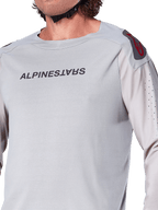 Närbild på Alpinestars A-Aria Polartec Switch långärmad tröja i Light Gray, med Alpinestars logotyp på bröstet, röd logotyp på axeln och laserperforerade ärmar för luftflöde, premium mountainbike-utrustning