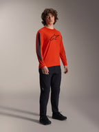 Manlig modell i Alpinestars A-Dura Insert Astar-tröja, långärmad, Spicy Orange med svart Astar-logotyp på bröstet, mörkgrå detaljer på ärmarna, svarta byxor, professionella MTB-cykelkläder