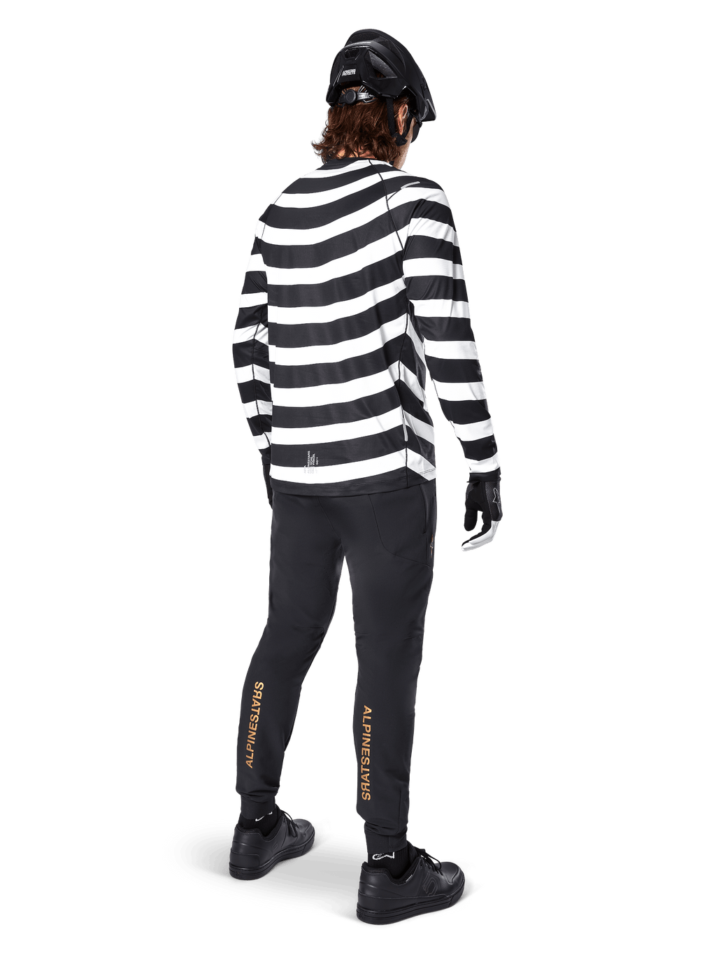 MTB rider wearing the Alpinestars A-Aria Oscar Long Sleeve Jersey, black and white horizontal spiral stripes, paired with black technical pants featuring gold logos on the calves, black helmet and shoes, complete off-road cycling outfit from behind