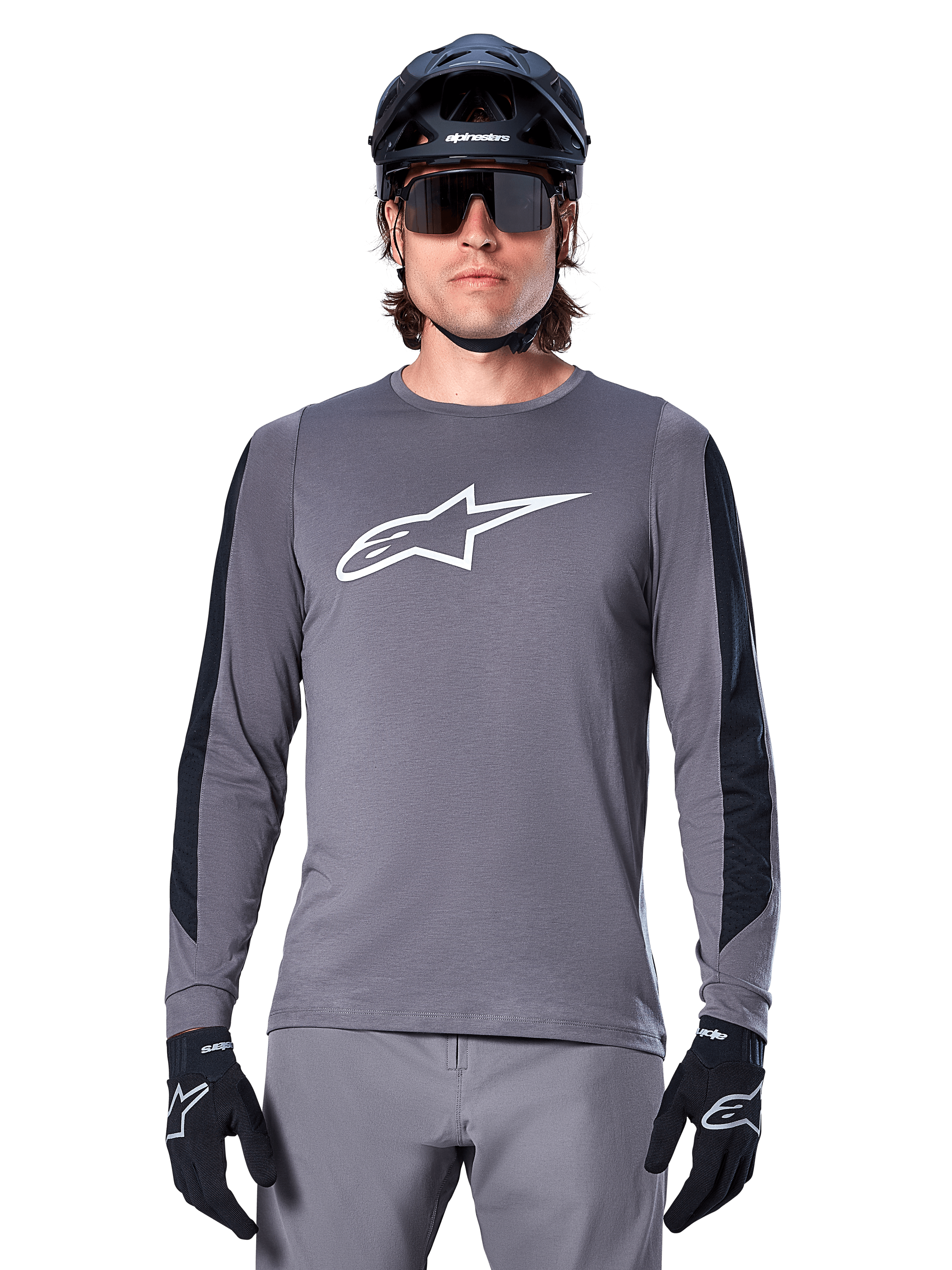 Alpinestars A-Dura Dri Astar långärmad tröja, mörkgrå, med en stor vit Astar-logotyp på bröstet och svarta meshpaneler på ärmarna, bärs av en cyklist med en svart mountainbikehjälm och sportglasögon, MTB-cykelkläder