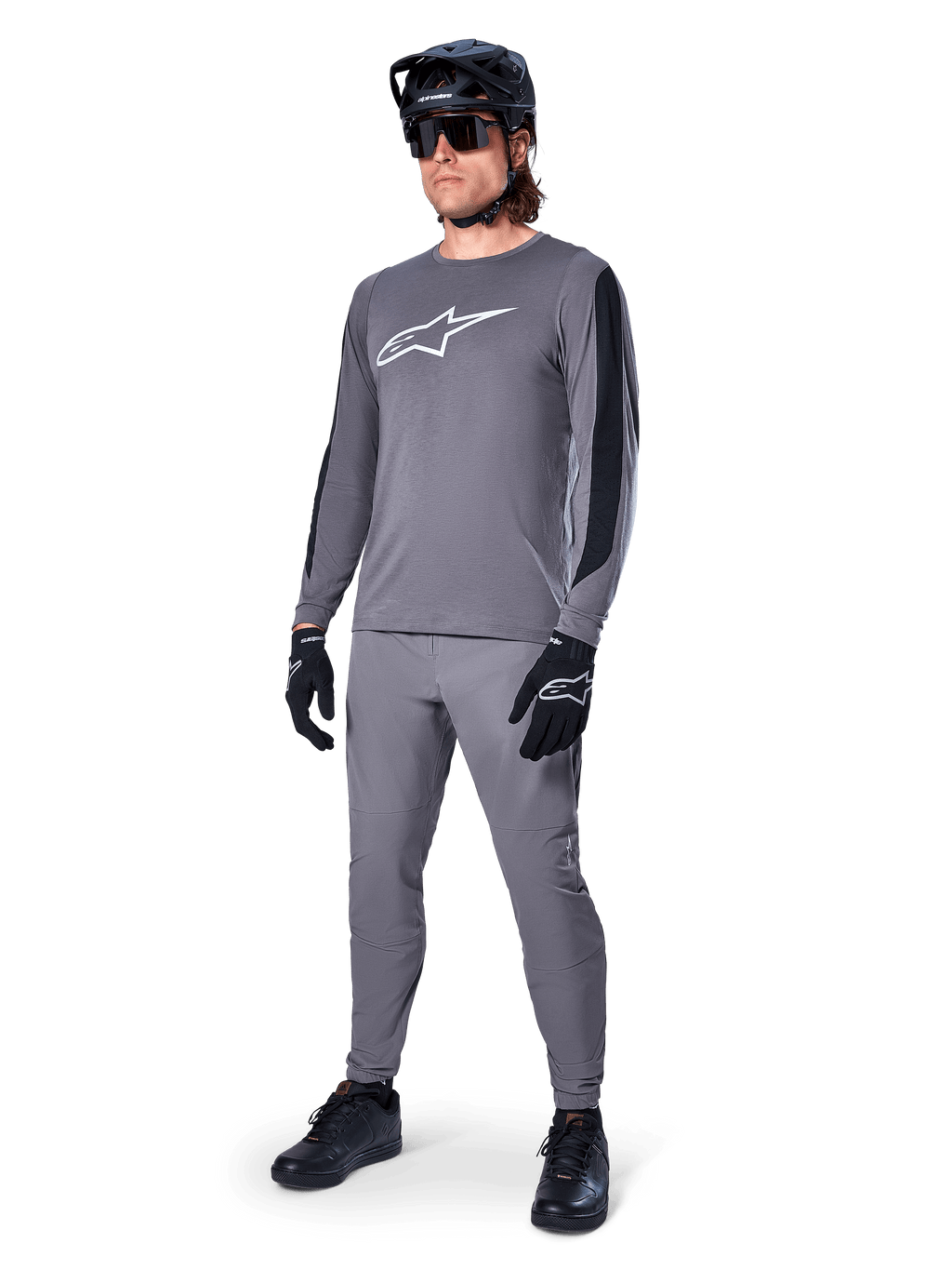 Alpinestars A-Dura Dri Astar-tröja, långärmad MTB-tröja, mörkgrå med vit bröstlogotyp, svarta meshpaneler på ärmarna, bärs med matchande gråa byxor, svart hjälm och handskar, högpresterande mountainbike-kläder