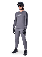 Alpinestars A-Dura Dri Astar-tröja, långärmad MTB-tröja, mörkgrå med vit bröstlogotyp, svarta meshpaneler på ärmarna, bärs med matchande gråa byxor, svart hjälm och handskar, högpresterande mountainbike-kläder