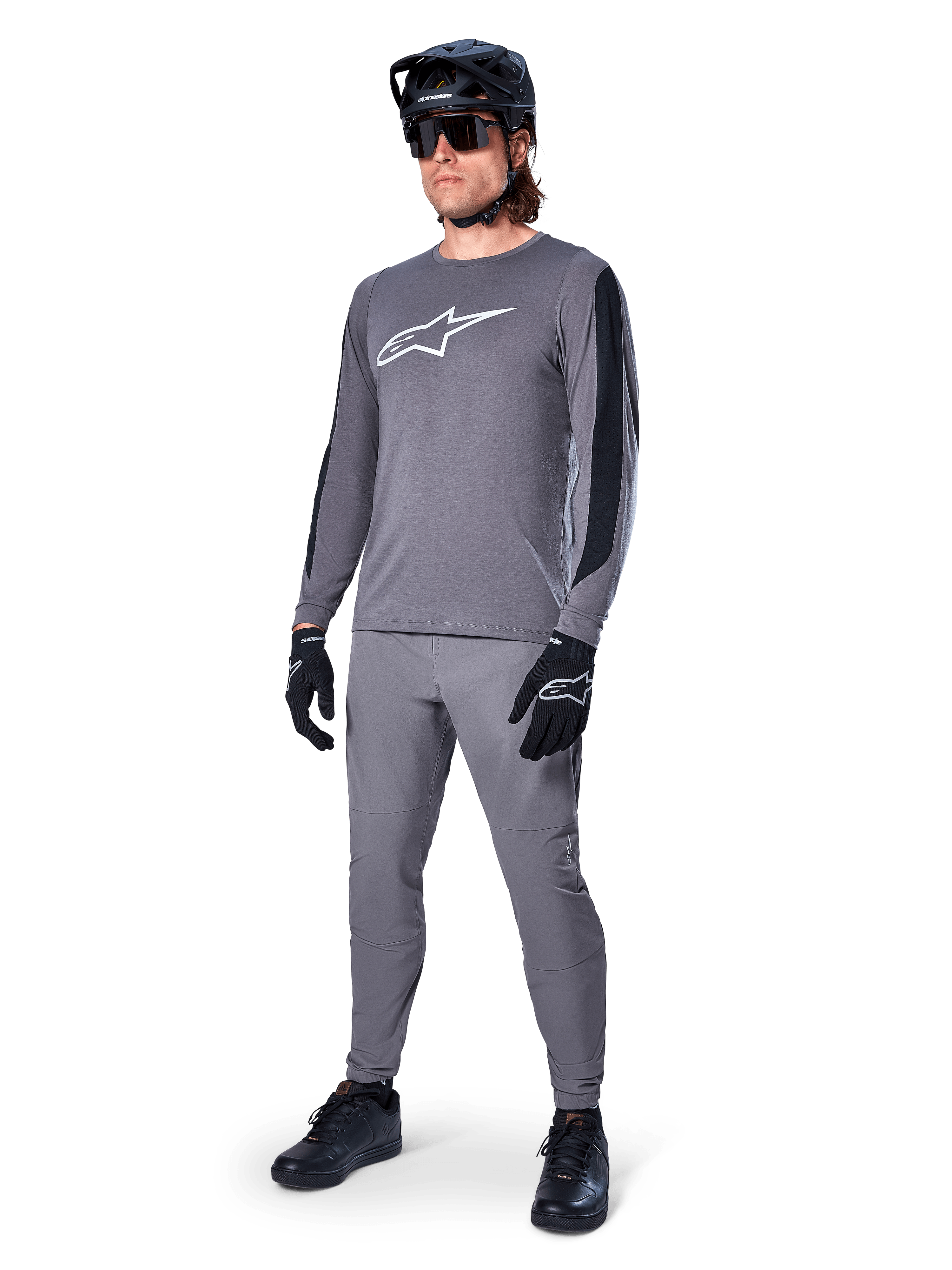 Alpinestars A-Dura Dri Astar-tröja, långärmad MTB-tröja, mörkgrå med vit bröstlogotyp, svarta meshpaneler på ärmarna, bärs med matchande gråa byxor, svart hjälm och handskar, högpresterande mountainbike-kläder