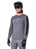 Alpinestars A-Dura Dri Astar långärmad tröja, mörkgrå med vit logotyp på bröstet och svarta meshpaneler på sidorna, MTB-cykeltröja, bärs med svart hjälm, solglasögon och matchande grå byxor
