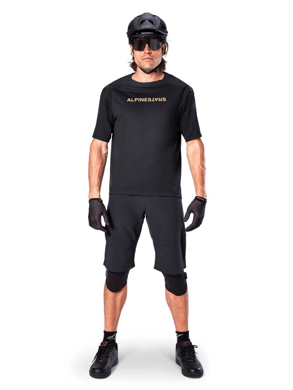 Alpinestars A-Aria Polartec Switch Jersey, Short Sleeve MTB Jersey, Black with tan lettering, worn with coordinated black mountain bike gear including helmet, shorts, and knee pads, performance off-road cycling apparel