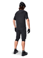 Male mountain bike rider from the back wearing the Alpinestars A-Aria Polartec Switch Jersey in black, short sleeve MTB jersey, paired with black mountain bike shorts, black helmet, and gloves, coordinated performance outfit for off-road trail riding