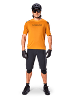 Manlig cyklist bär Alpinestars A-Aria Polartec Switch kortärmad tröja i Dark Gold, kombinerat med svarta MTB-shorts, hjälm, solglasögon och handskar, professionell mountainbike-utrustning