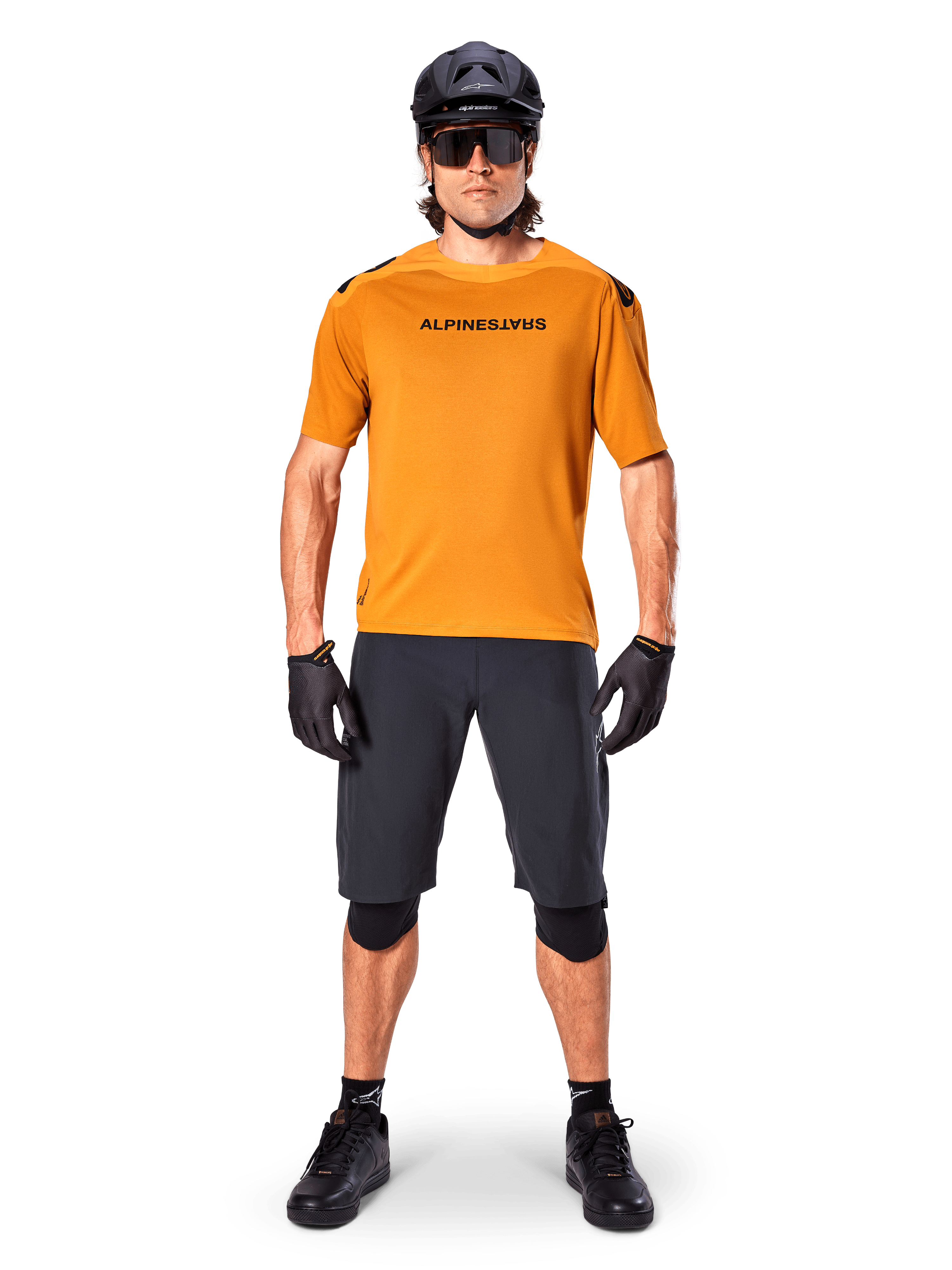 Manlig cyklist bär Alpinestars A-Aria Polartec Switch kortärmad tröja i Dark Gold, kombinerat med svarta MTB-shorts, hjälm, solglasögon och handskar, professionell mountainbike-utrustning