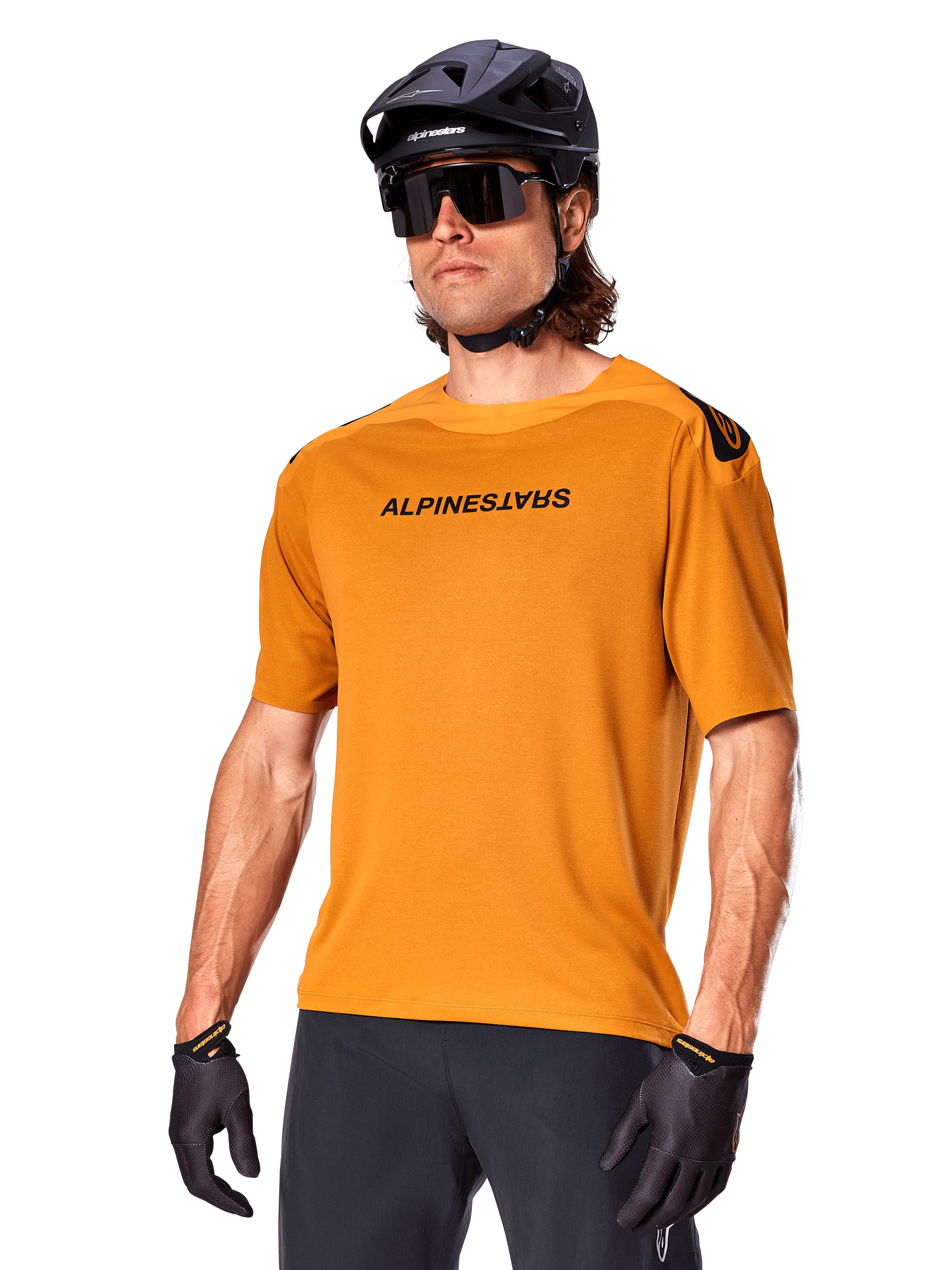 Alpinestars A-Aria Polartec Switch Jersey, kortärmad MTB-tröja, Dark Gold med svart logotyp, bärs av modell med svart hjälm, solglasögon och cykelhandskar, högpresterande mountainbike-kläder