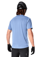 Alpinestars A-Dura Dri Astar kortärmad tröja, MTB-tröja, Infinity Blue, baksida som visar nätpaneler för ventilation på axlarna och en förlängd rygg, bärs med en svart MTB-hjälm och handskar, prestanda-cykelutrustning