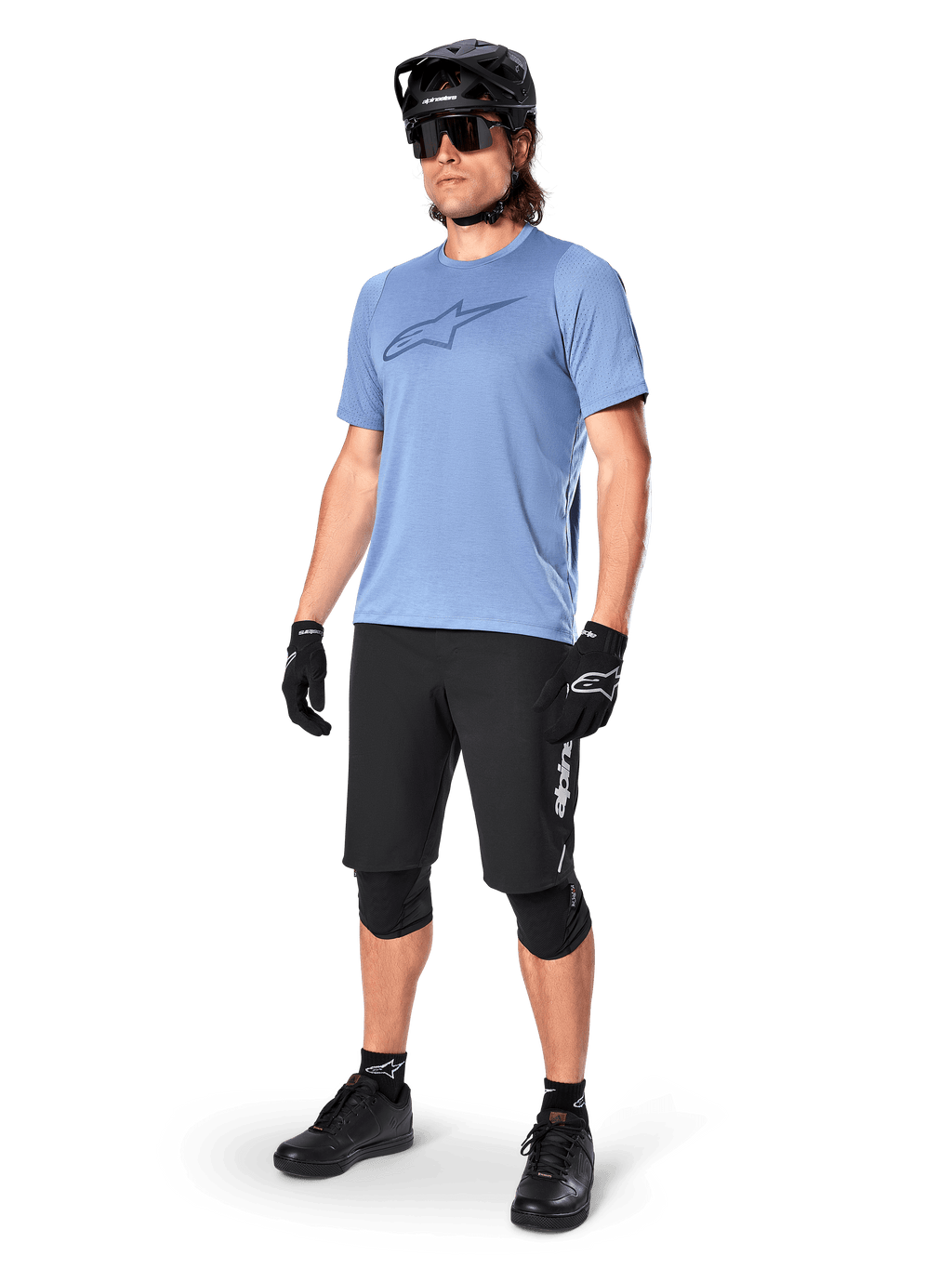 Manlig cyklist bär Alpinestars A-Dura Dri Astar kortärmad tröja i Infinity Blue, svarta MTB-shorts, svart hjälm, solglasögon, knäskydd och handskar, komplett outfit för mountainbike
