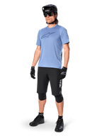 Manlig cyklist bär Alpinestars A-Dura Dri Astar kortärmad tröja i Infinity Blue, svarta MTB-shorts, svart hjälm, solglasögon, knäskydd och handskar, komplett outfit för mountainbike