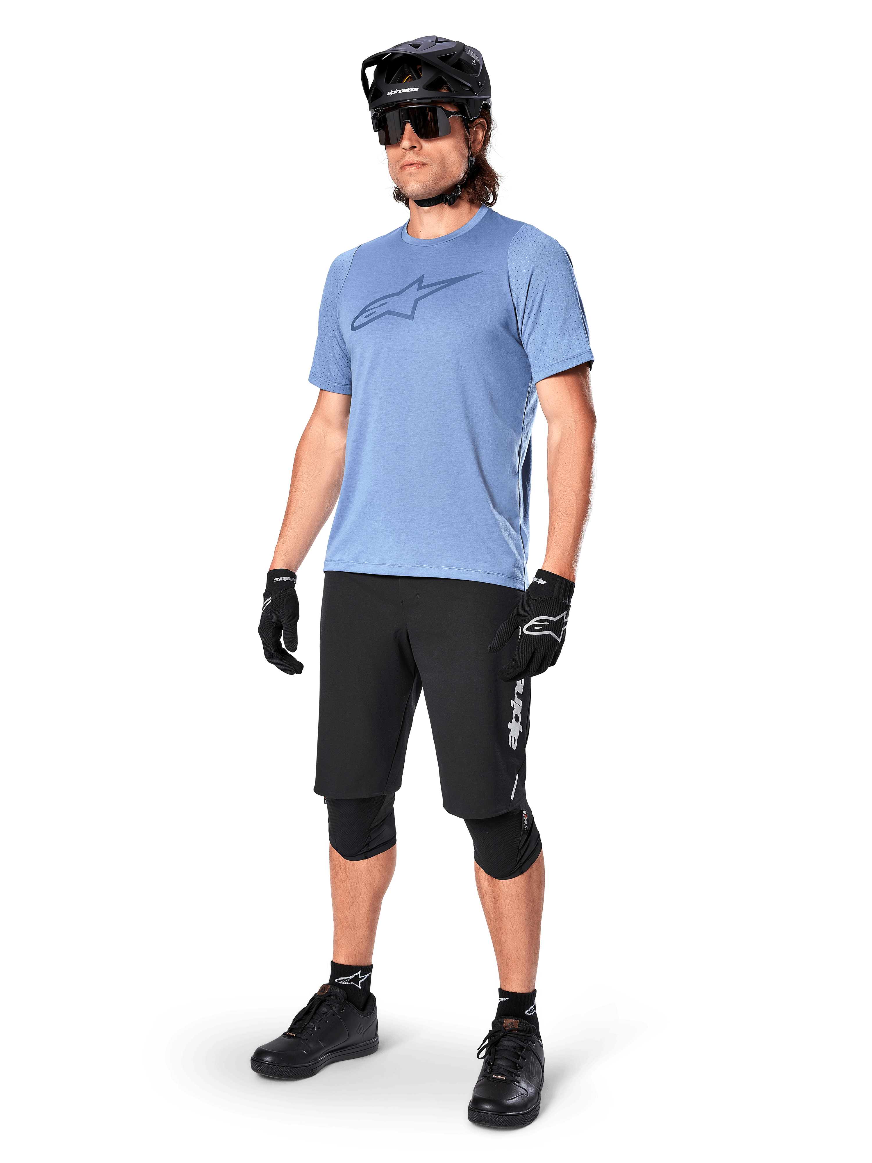 Manlig cyklist bär Alpinestars A-Dura Dri Astar kortärmad tröja i Infinity Blue, svarta MTB-shorts, svart hjälm, solglasögon, knäskydd och handskar, komplett outfit för mountainbike