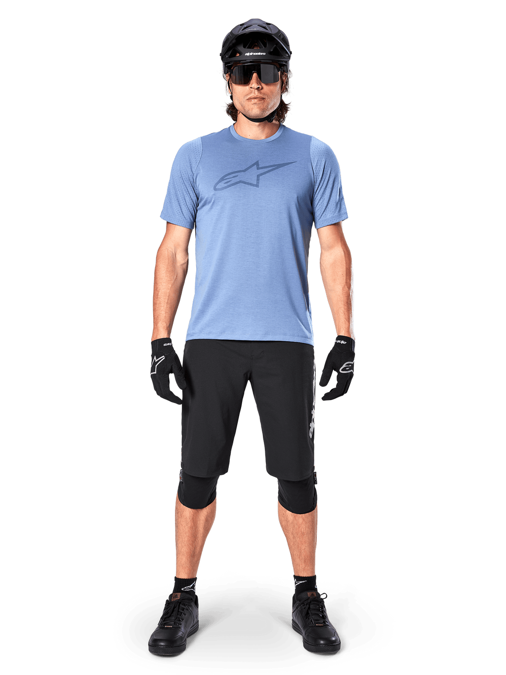 Manlig mountainbikecyklist som bär Alpinestars A-Dura Dri Astar kortärmad tröja i Infinity Blue, med en framträdande Astars-logotyp på bröstet, matchad med svarta MTB-shorts, svart hjälm, solglasögon och skyddsutrustning för terrängcykling