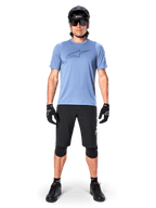Manlig mountainbikecyklist som bär Alpinestars A-Dura Dri Astar kortärmad tröja i Infinity Blue, med en framträdande Astars-logotyp på bröstet, matchad med svarta MTB-shorts, svart hjälm, solglasögon och skyddsutrustning för terrängcykling