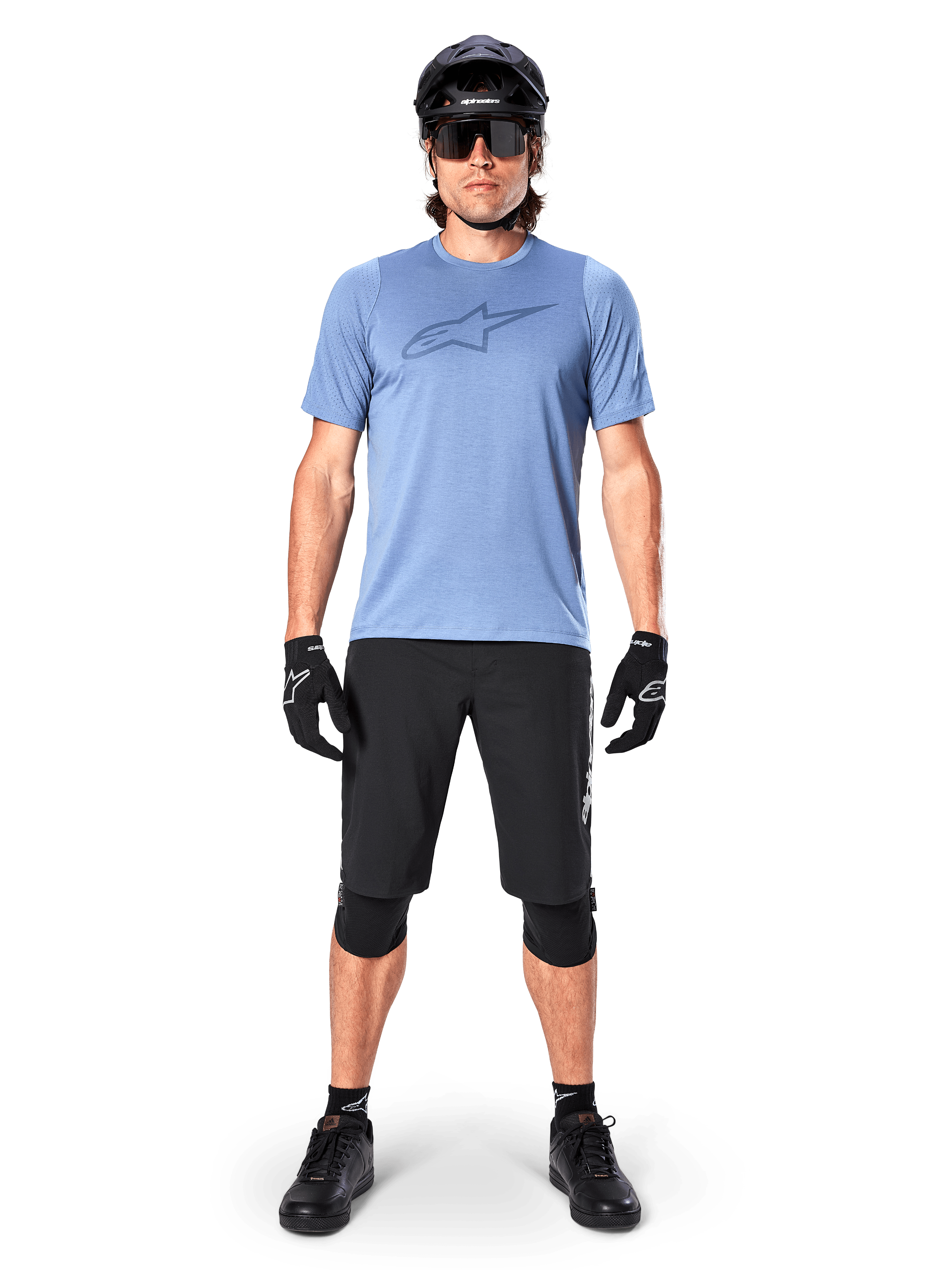 Manlig mountainbikecyklist som bär Alpinestars A-Dura Dri Astar kortärmad tröja i Infinity Blue, med en framträdande Astars-logotyp på bröstet, matchad med svarta MTB-shorts, svart hjälm, solglasögon och skyddsutrustning för terrängcykling