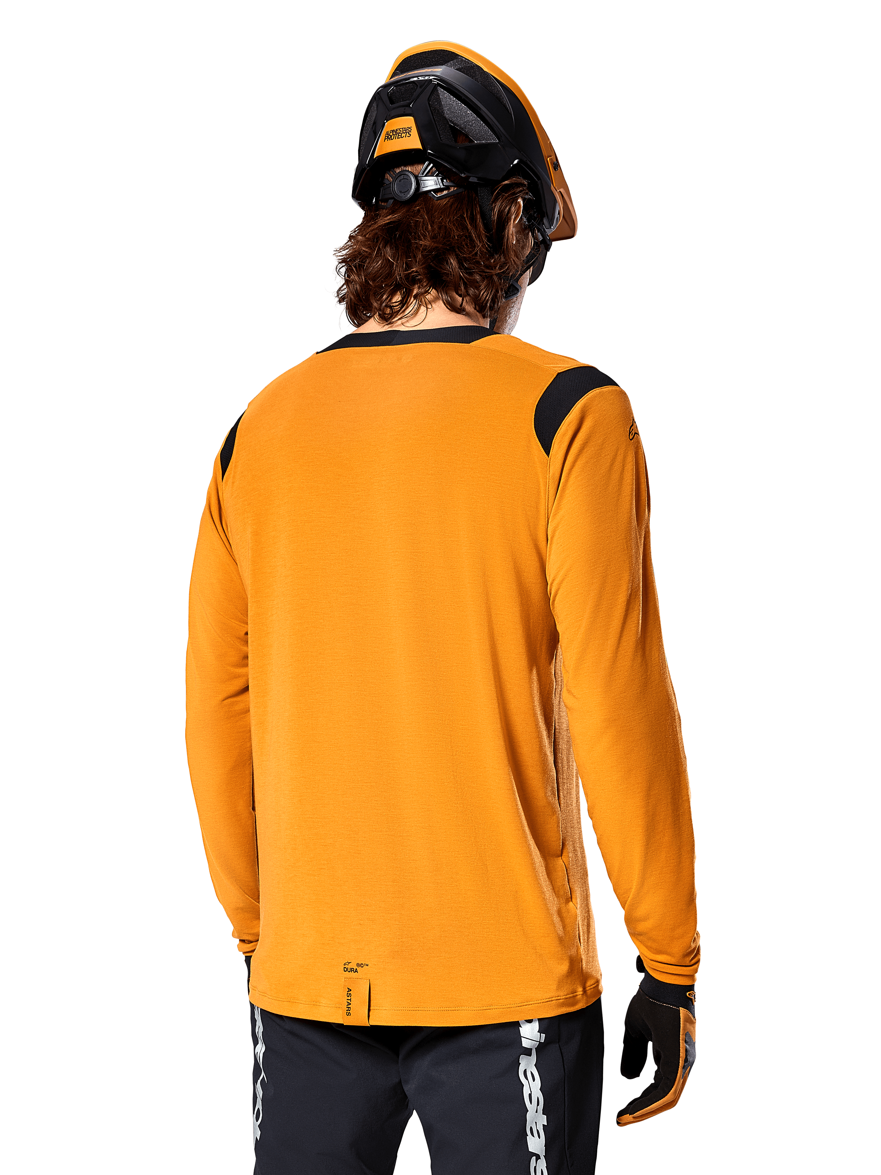 Alpinestars A-Dura Dri Wool långärmad tröja i Dark Gold, sedd bakifrån på en cyklist med mountainbikehjälm och handskar, svarta meshpaneler på axlarna och ett längre ryggslut, tekniska cykelkläder för trailcykling