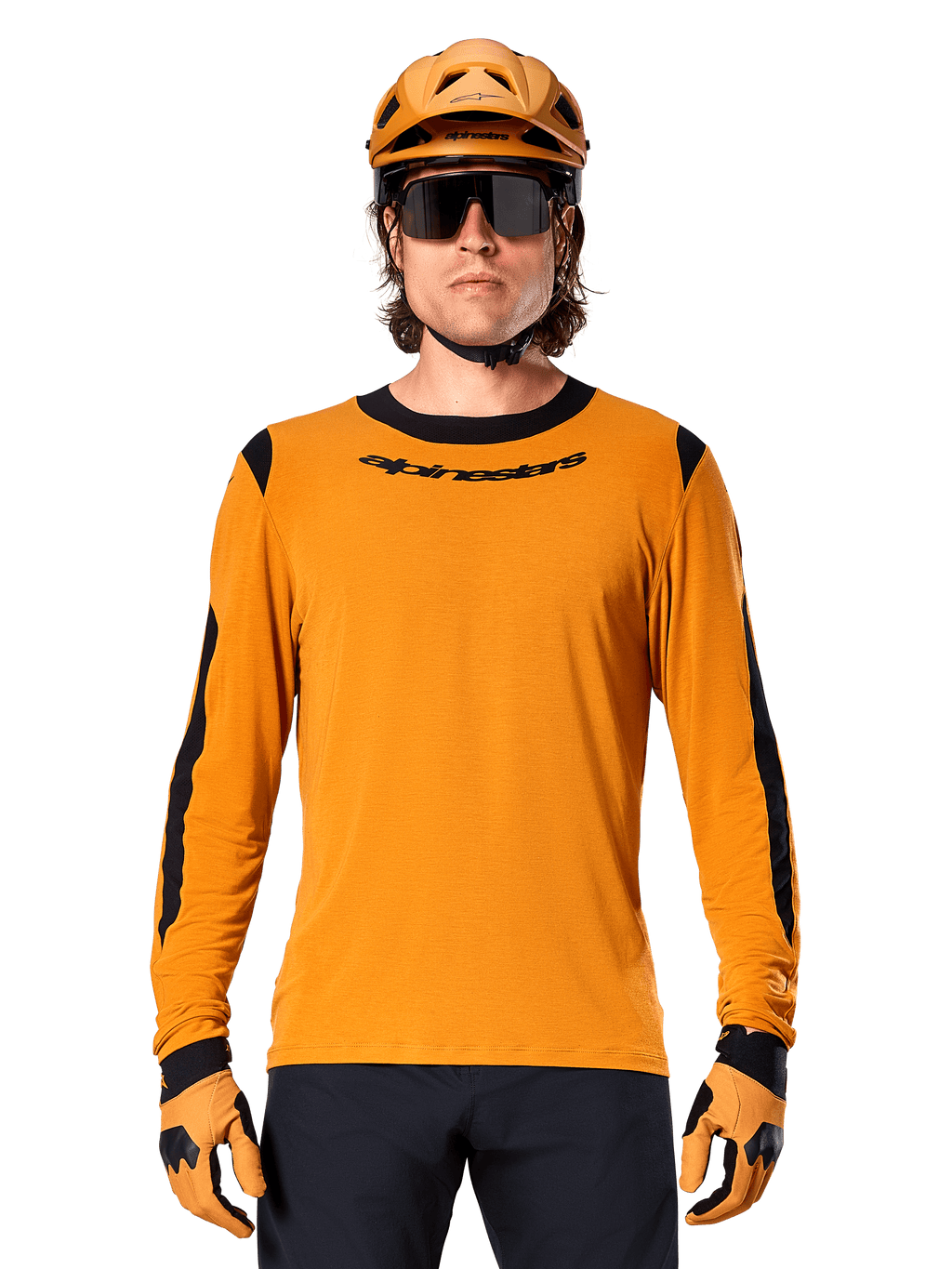 Manlig modell bär Alpinestars A-Dura Dri Wool Long Sleeve Jersey i Dark Gold, matchad med en matchande guld-MTB-hjälm och handskar, svarta meshpaneler på axlar och ärmar, svart Alpinestars-logotyp på bröstet, mörka solglasögon och byxor, tekniska mountainbikekläder