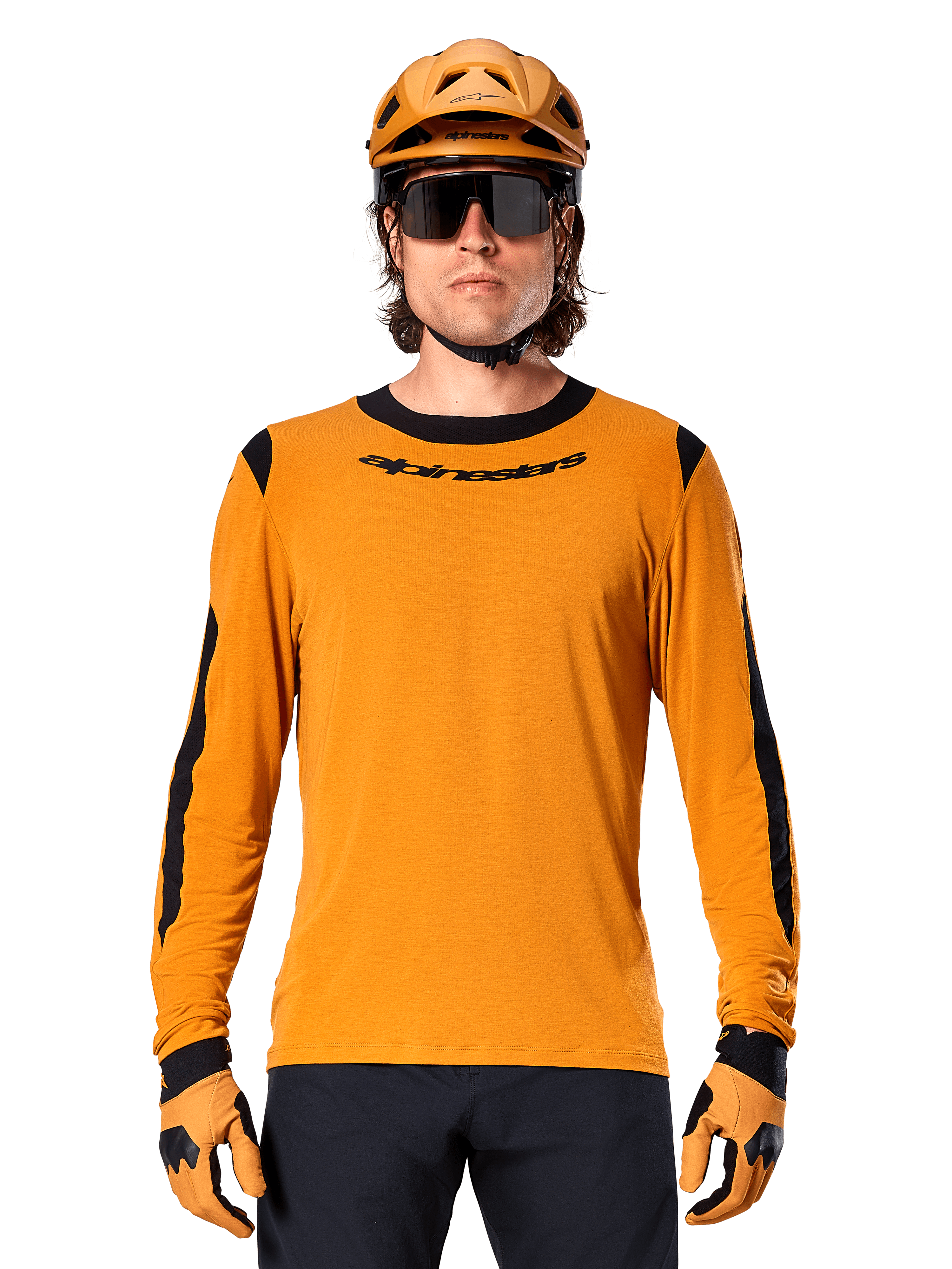 Manlig modell bär Alpinestars A-Dura Dri Wool Long Sleeve Jersey i Dark Gold, matchad med en matchande guld-MTB-hjälm och handskar, svarta meshpaneler på axlar och ärmar, svart Alpinestars-logotyp på bröstet, mörka solglasögon och byxor, tekniska mountainbikekläder