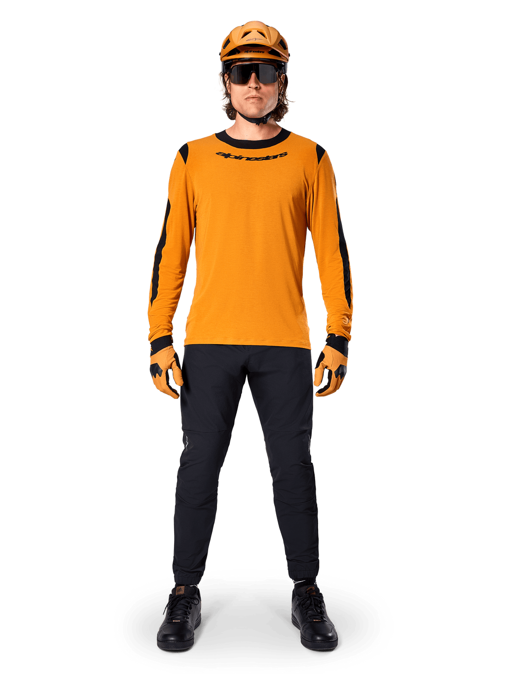 Mountainbike-cyklist bär Alpinestars A-Dura Dri Wool Long Sleeve Jersey, mörkguld med svarta detaljer på krage och ärmar, kombinerat med svarta byxor, matchande guldfärgad hjälm och handskar samt svarta solglasögon, professionell mountainbike-utrustning
