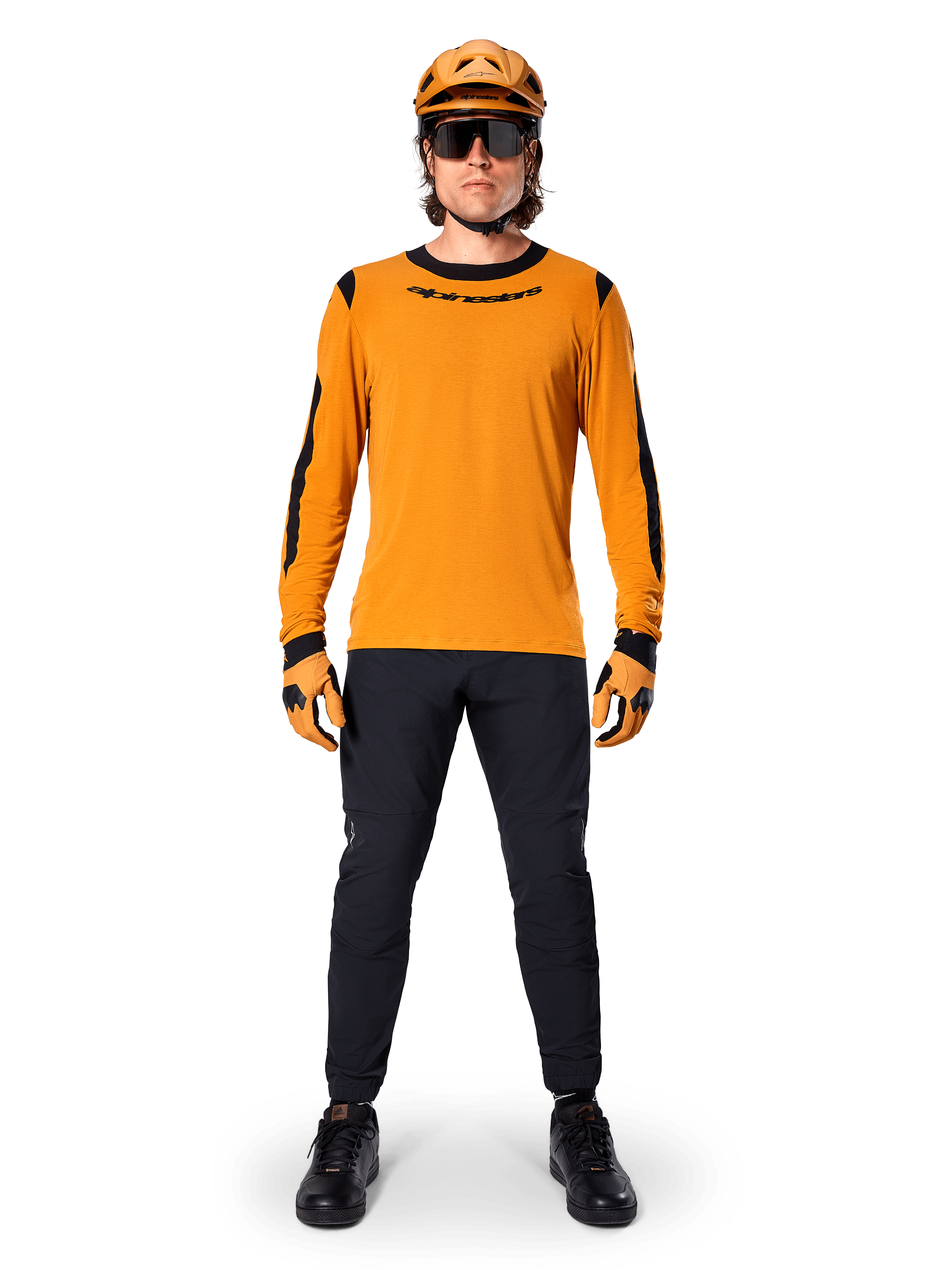 Mountainbike-cyklist bär Alpinestars A-Dura Dri Wool Long Sleeve Jersey, mörkguld med svarta detaljer på krage och ärmar, kombinerat med svarta byxor, matchande guldfärgad hjälm och handskar samt svarta solglasögon, professionell mountainbike-utrustning