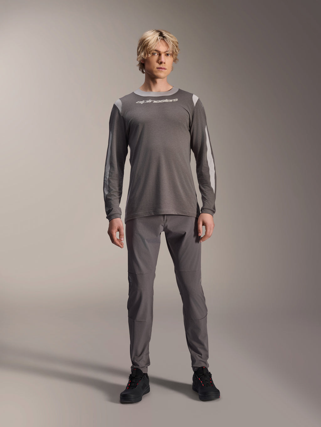 Alpinestars A-Dura Dri Wool Long Sleeve Jersey, Dark Gray, worn by model with matching gray pants and black shoes, white Alpinestars branding on chest, light gray mesh panels on shoulders and sleeves, technical mountain bike gear