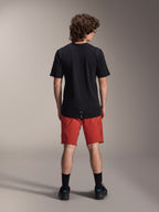 Manlig modell sedd bakifrån i Alpinestars A-Dura Elite-shorts i Dark Orange och en svart kortärmad A-Dura Dri Wool-tröja, svarta strumpor och cykelskor, professionella mountainbikekläder