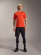 Alpinestars A-Aria Astar kortärmad tröja, Spicy Orange, buren av modell med svarta mountainbikeshorts och knäskydd, lätt och andningsbart prestandaplagg för MTB