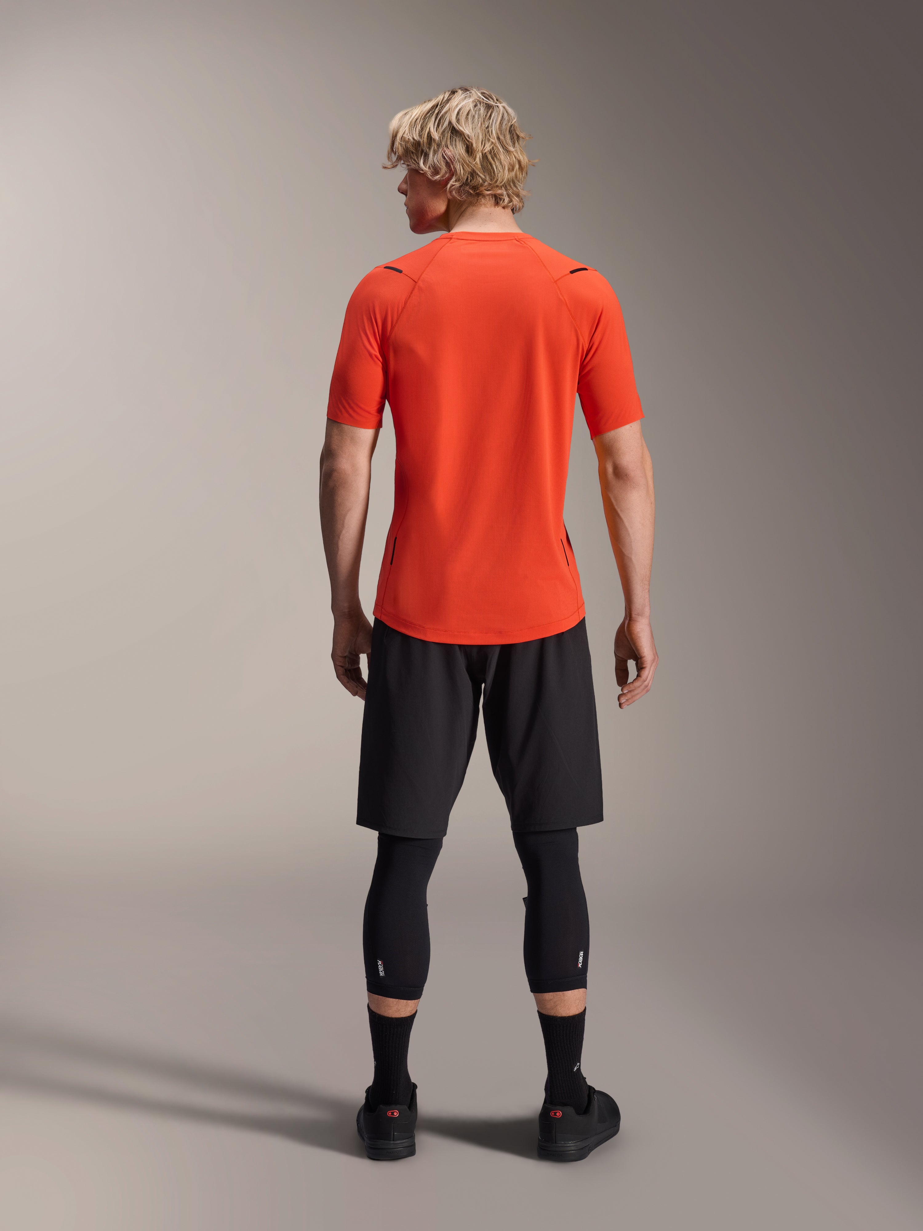 Alpinestars A-Aria Astar tröja, kortärmad MTB-tröja, Spicy Orange, vy bakifrån som visar prestandapassform och förlängt ryggslut, kombinerad med svarta cykelshorts och leggings