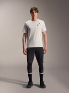 Manlig modell iklädd Alpinestars A-Aria Astar kortärmad tröja i Ecru, matchad med svarta MTB-shorts, knäskydd och svarta cykelskor, med en minimalistisk svart stjärnlogotyp på bröstet, designad för terräng- och stigcykling.