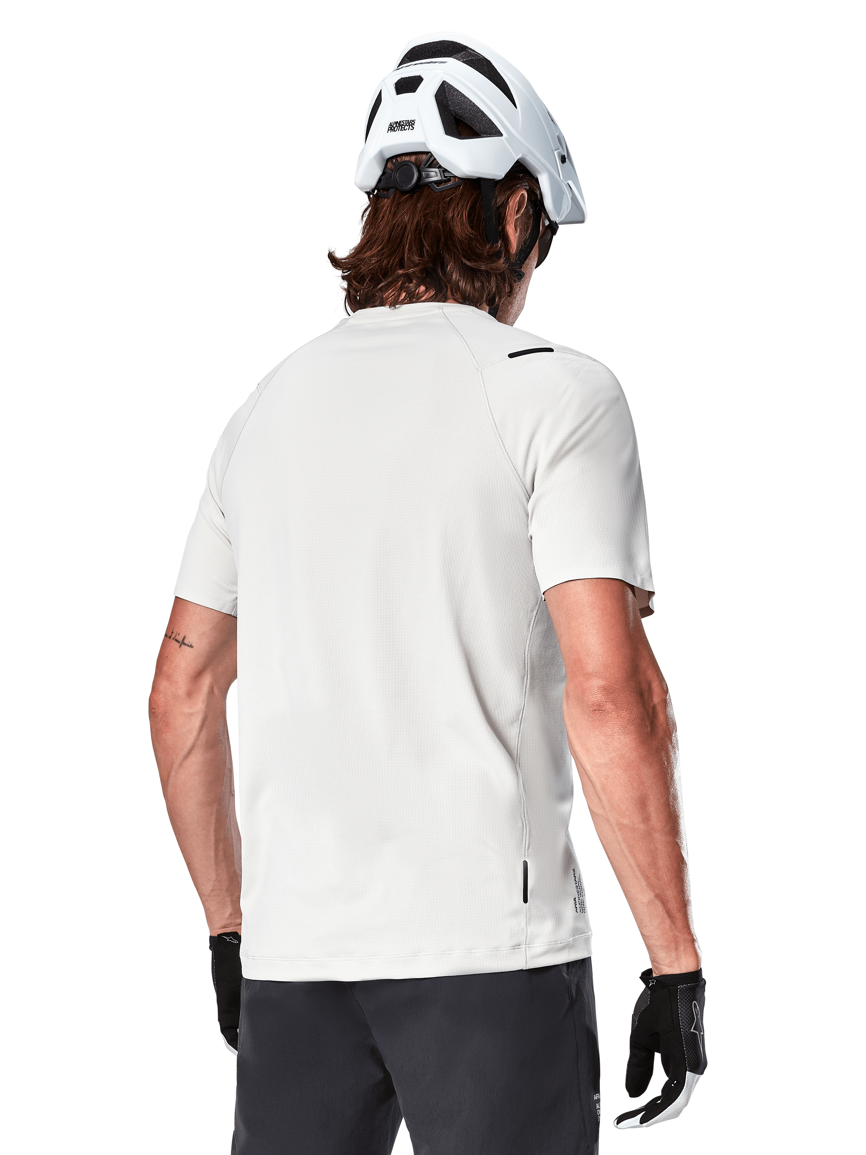 Alpinestars A-Aria Astar Jersey, kortärmad, White Dove, vy bakifrån av en lätt och andningsbar mountainbike-tröja, bärs med en vit hjälm och svarta cykelhandskar, med ett förlängt bakstycke för extra täckning