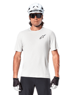 Cyklist som bär Alpinestars A-Aria Astar kortärmad tröja, White Dove med liten svart Astar-logotyp på bröstet, vit cykelhjälm, svarta solglasögon och svartvita handskar, prestanda-MTB-utrustning för terrängkörning