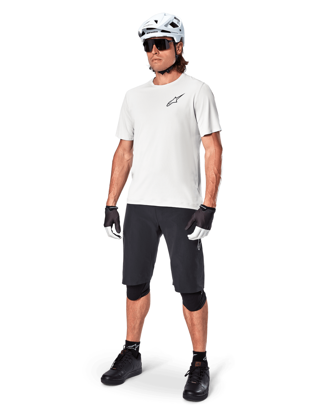 MTB-cyklist iklädd Alpinestars A-Aria Astar kortärmad tröja i White Dove, kombinerad med svarta mountainbikeshorts, vit hjälm och svarta knäskydd, med en liten svart logotyp på bröstet, matchande cykelutrustning för stigcykling