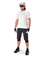 MTB-cyklist iklädd Alpinestars A-Aria Astar kortärmad tröja i White Dove, kombinerad med svarta mountainbikeshorts, vit hjälm och svarta knäskydd, med en liten svart logotyp på bröstet, matchande cykelutrustning för stigcykling