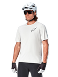 Alpinestars A-Aria Astar kortärmad tröja, White Dove, bärs av en cyklist med vit hjälm och mörka solglasögon, med en liten svart stjärnlogotyp på bröstet, ventilerande funktionsplagg för mountainbike