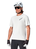 Alpinestars A-Aria Astar kortärmad tröja, White Dove, bärs av en cyklist med vit hjälm och mörka solglasögon, med en liten svart stjärnlogotyp på bröstet, ventilerande funktionsplagg för mountainbike