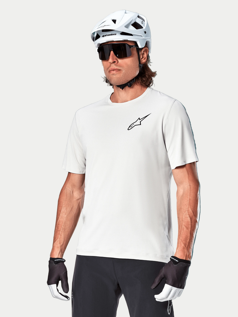 Alpinestars A-Aria Astar Short Sleeve Jersey, White Dove, worn by a cyclist with a white helmet and dark sunglasses, featuring a small black star logo on the chest, breathable performance gear for mountain biking