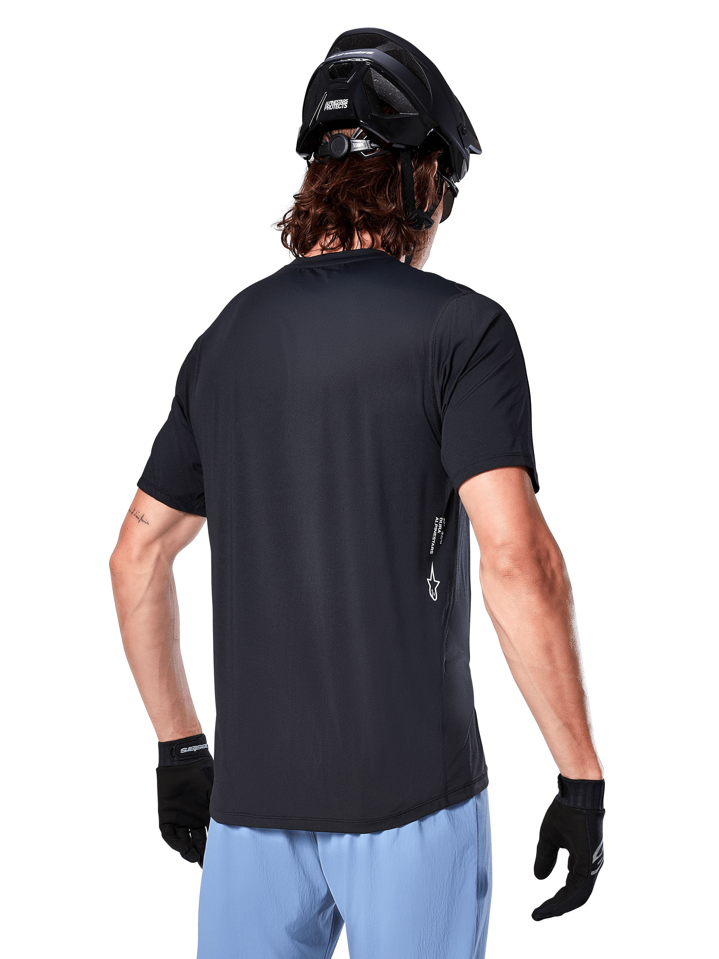 Alpinestars A-Dura Oscar Jersey, kortärmad cykeltröja, svart, baksida på cyklist, kombinerad med ljusblå shorts och svart MTB-hjälm, liten vit logotyp på sidan, funktionskläder för mountainbike