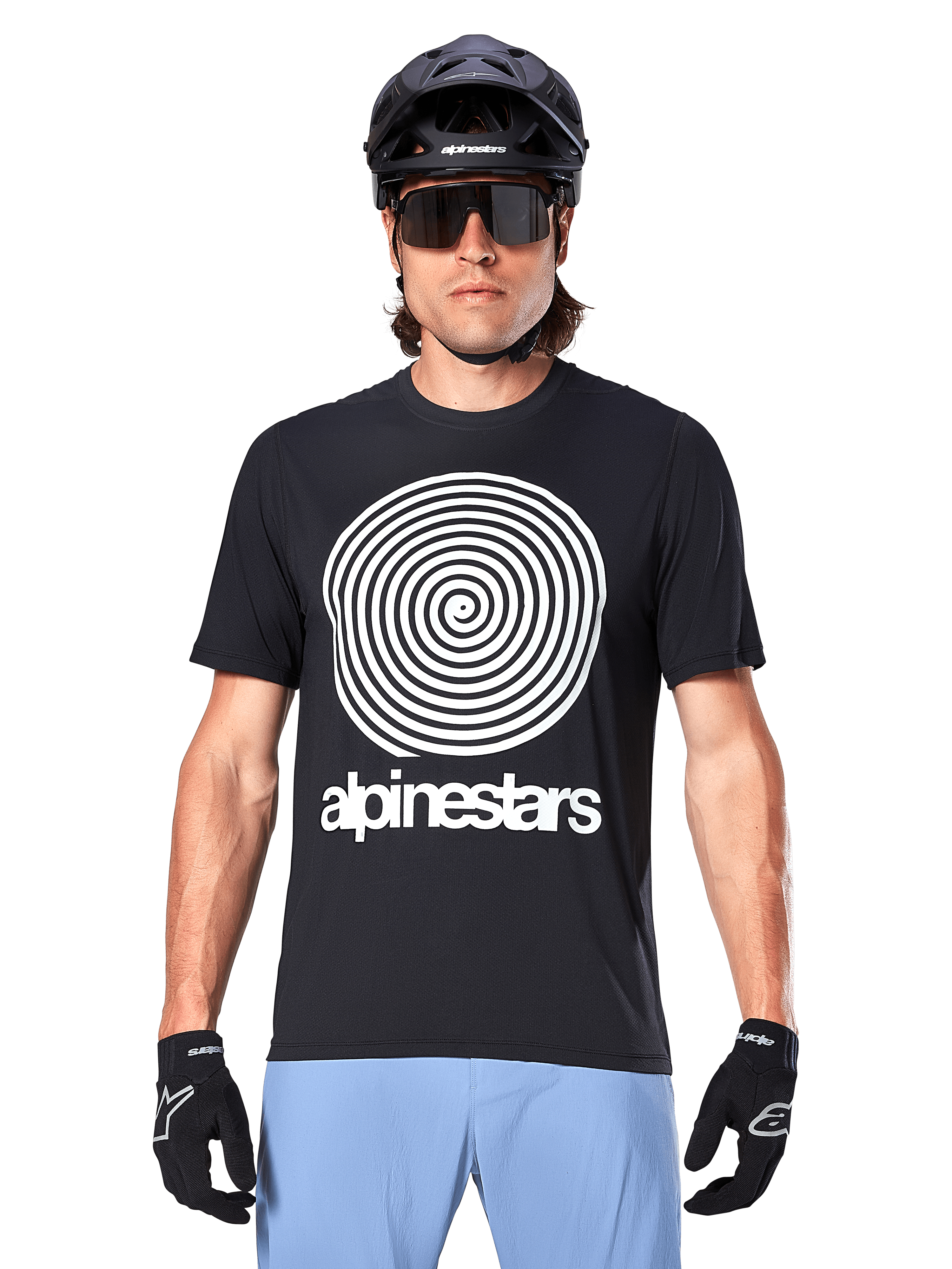 Alpinestars A-Dura Oscar-tröja, kortärmad MTB-tröja, svart med en stor vit vintage Oscar-spiralgrafik på bröstet, bärs med en svart cykelhjälm, solglasögon, svarta handskar och ljusblå shorts, heritage-inspirerad utrustning för terrängcykling