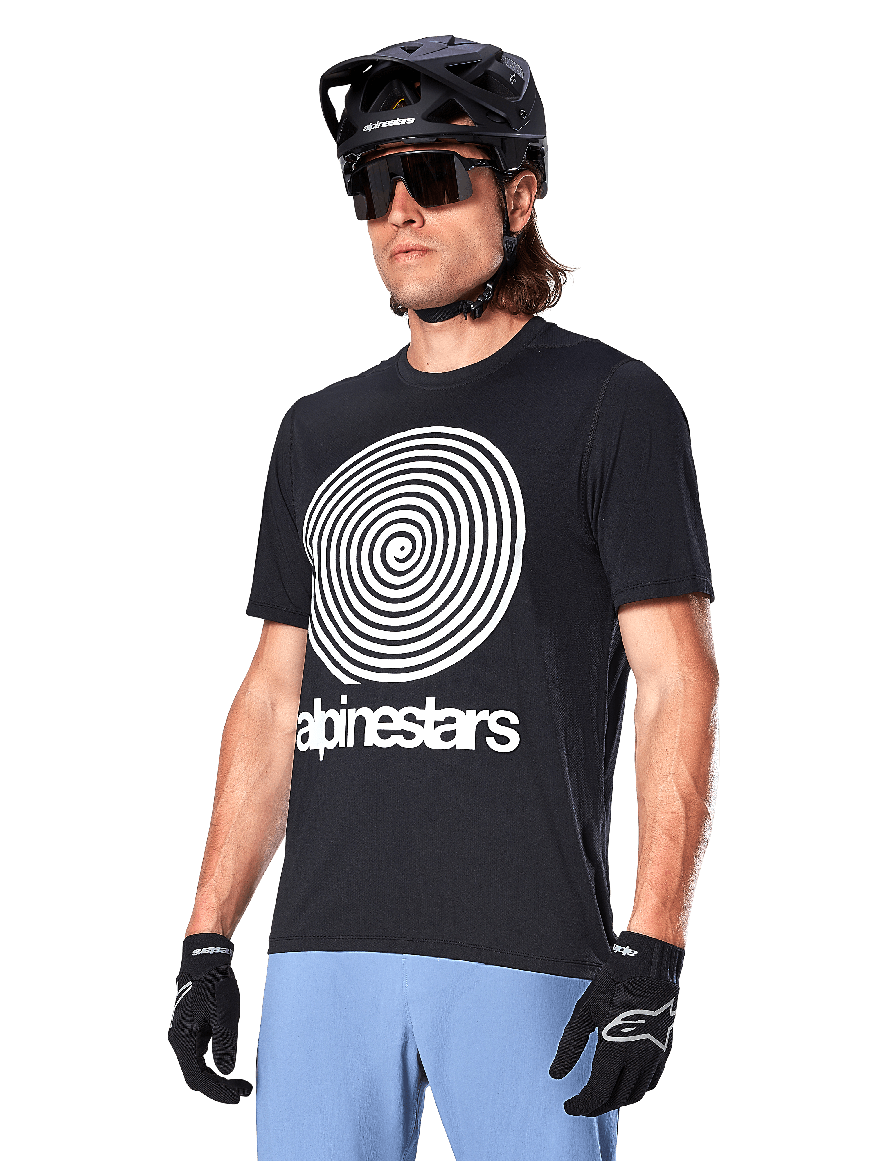 Alpinestars A-Dura Oscar-tröja - kortärmad, svart, med en stor vit spiralgrafik och Alpinestars-logotyp på bröstet, buren av en cyklist med svart MTB-hjälm, solglasögon och ljusblå byxor