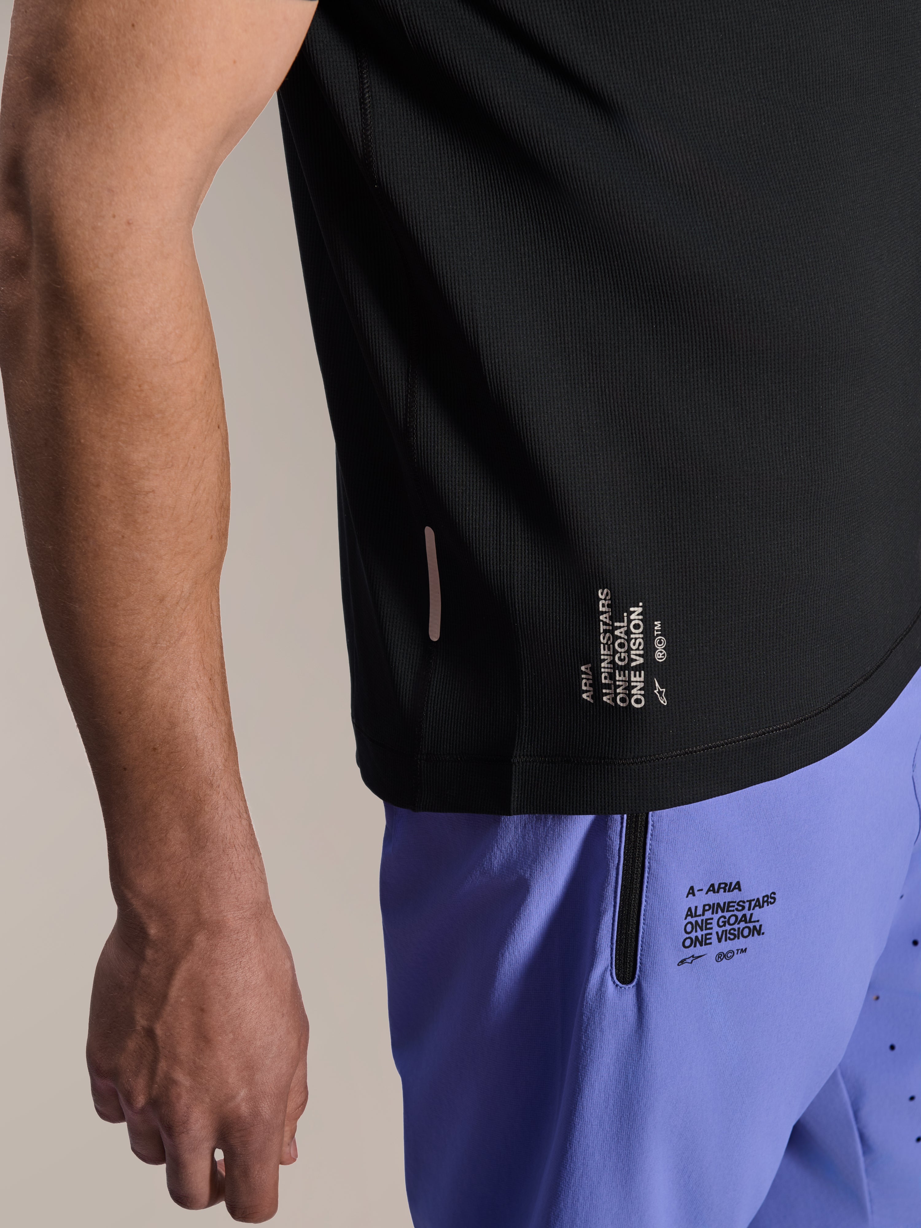 Alpinestars A-Aria Switch kortärmad tröja, svart MTB-tröja, närbild på sidsömmen med vit 'ONE GOAL. ONE VISION.'-grafik, bärs med ljuslila cykelshorts med matchande logotyper