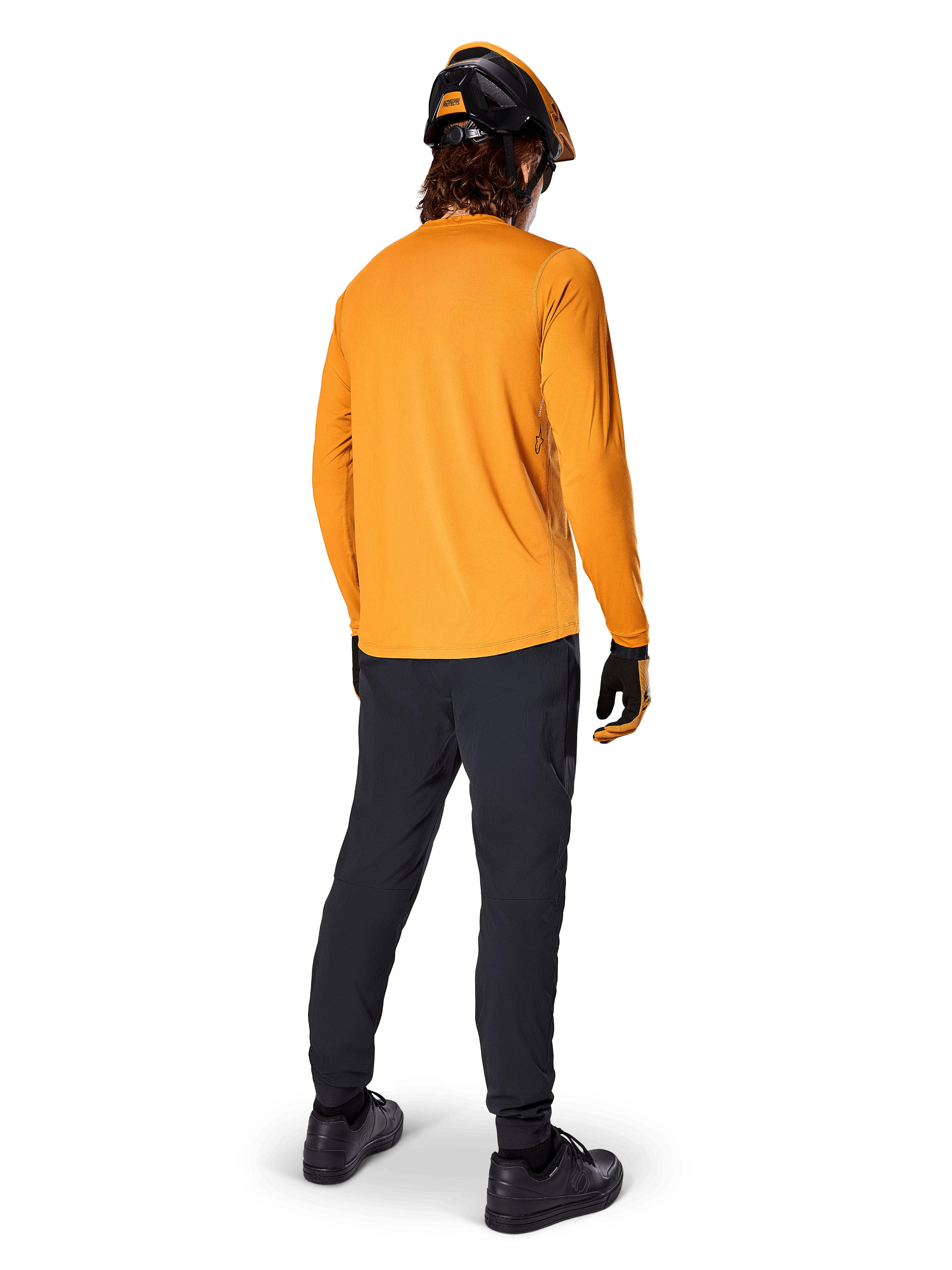 Mountain bike rider seen from behind wearing the Alpinestars A-Dura Rocker Long Sleeve Jersey in Dark Gold, black pants, orange and black helmet, and black shoes, coordinated performance MTB gear for trail riding