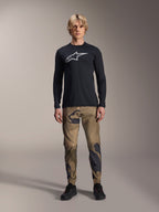 Alpinestars A-Dura Astar långärmad tröja, svart, med en stor vit Astars-logotyp på bröstet, bärs med kamouflagebyxor och svarta skor, avslappnade funktionskläder för mountainbike